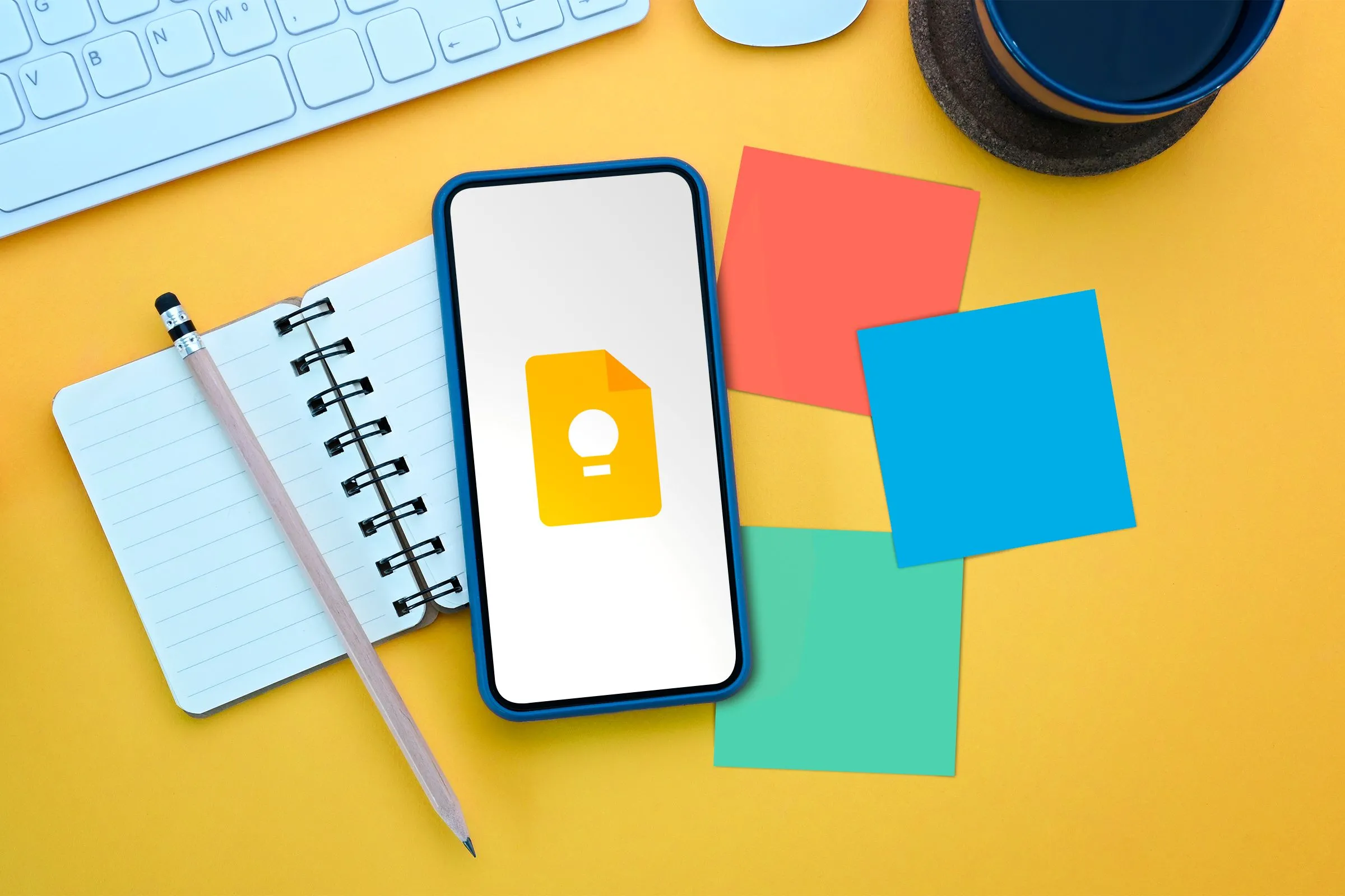 Điện thoại di động đặt trên cuốn sổ ghi chú mở, cùng với logo Google Keep và các mảnh giấy note nhiều màu sắc, tượng trưng cho khả năng ghi chú và tổ chức của ứng dụng.