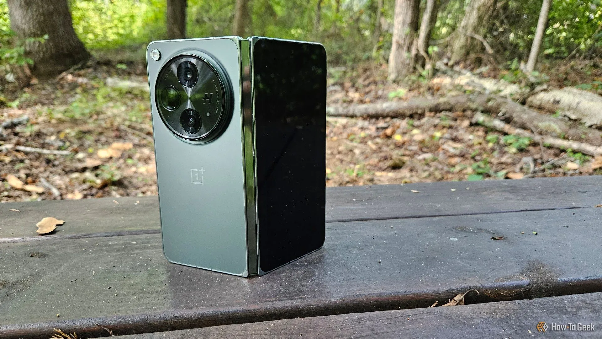 Điện thoại gập OnePlus Open đang mở đứng trên băng ghế, cho thấy kích thước màn hình ngoài và thiết kế ấn tượng.