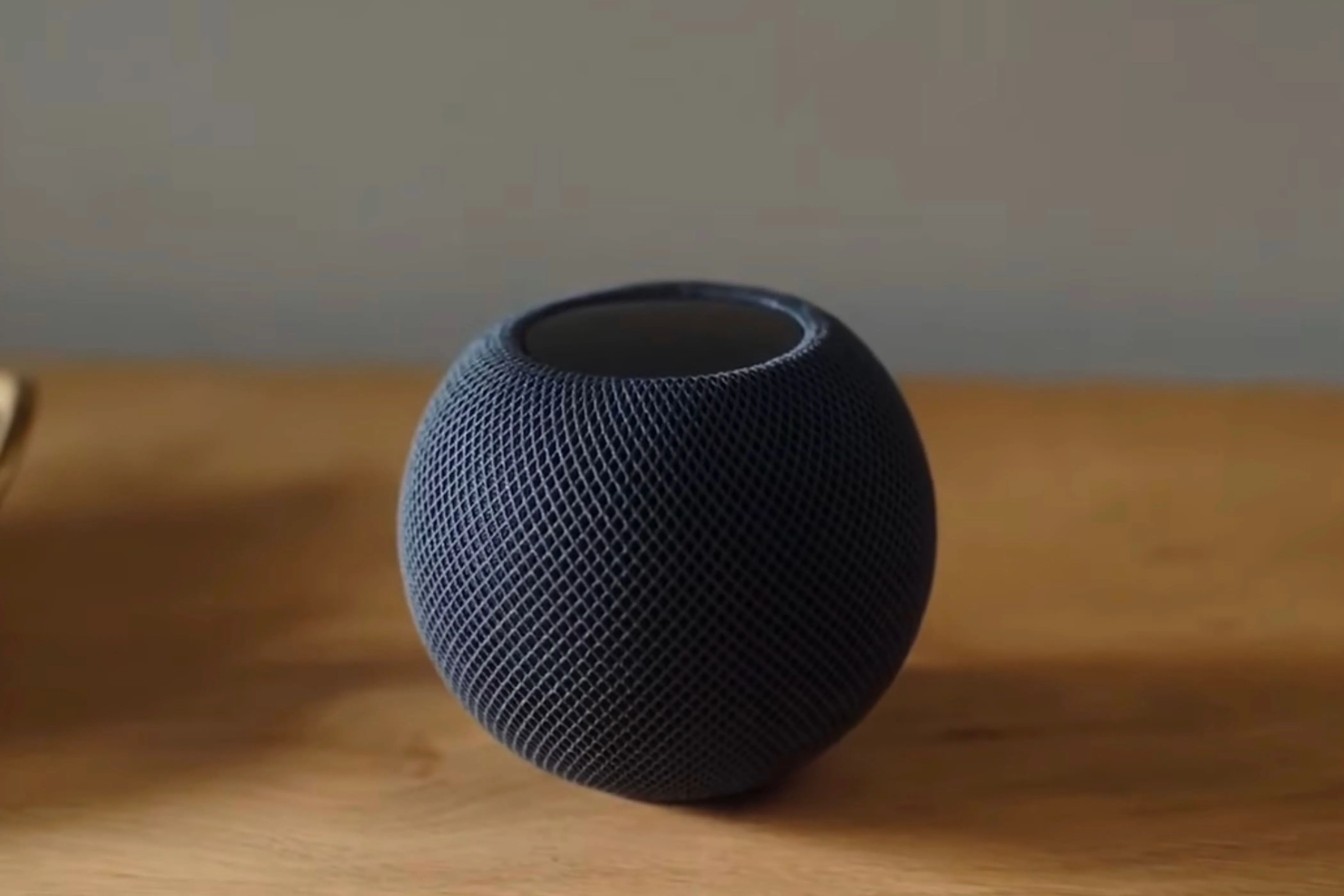 Loa thông minh HomePod Mini màu đen đặt trên mặt bàn gỗ với nền mờ.