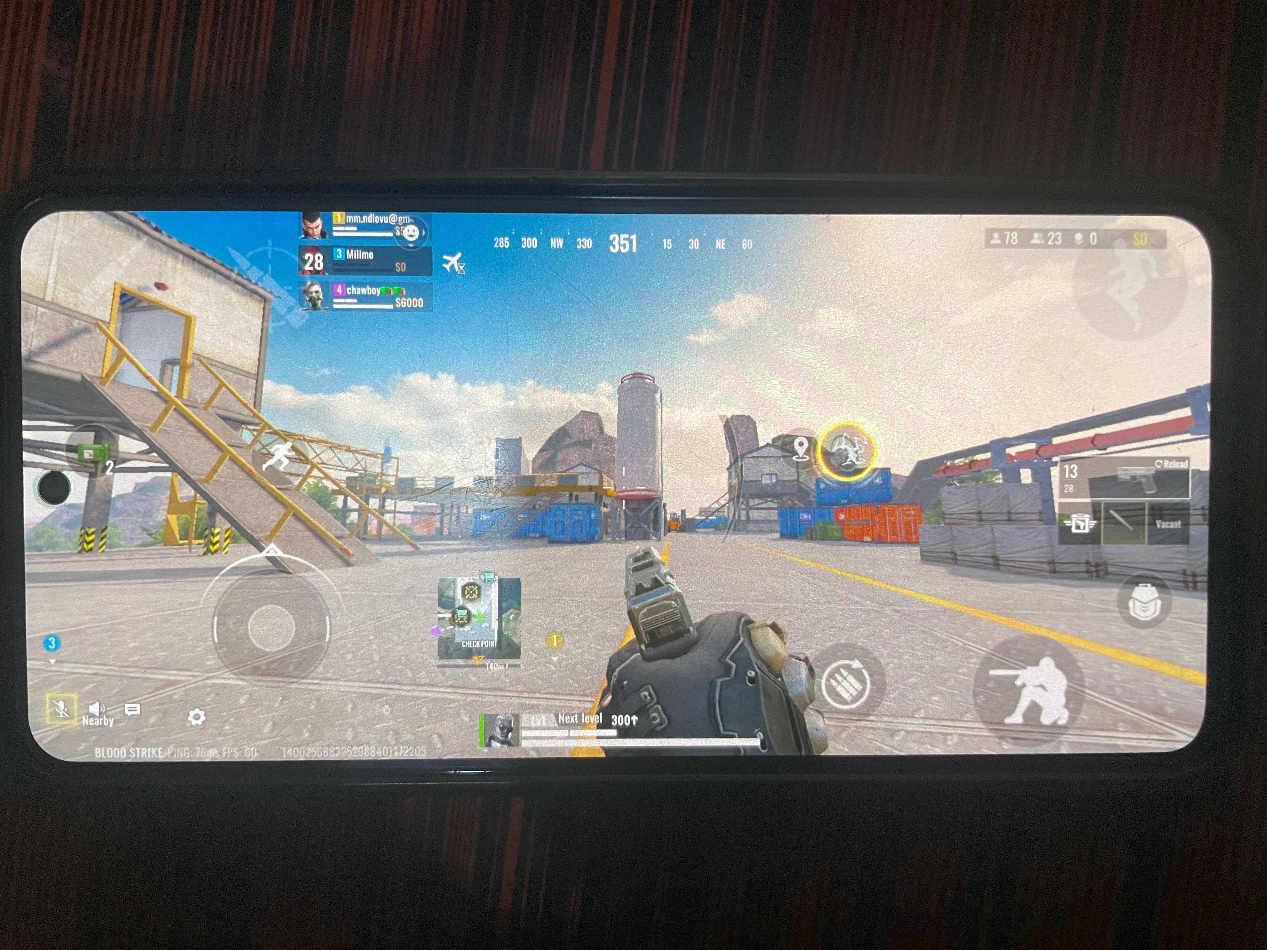 Màn hình điện thoại hiển thị giao diện game Blood Strike bị che khuất bởi ngón tay và các nút điều khiển.