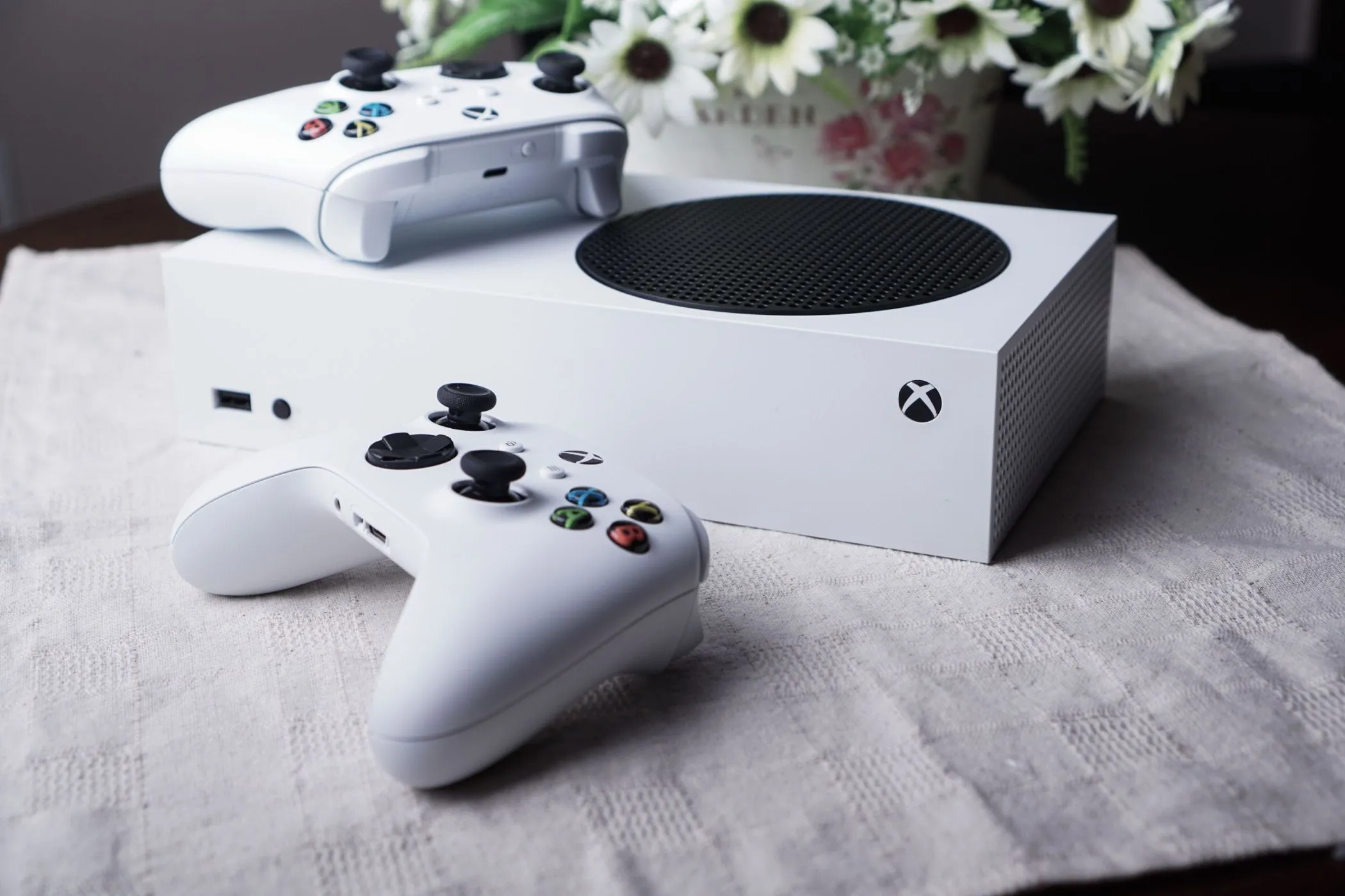 Máy console Series S đặt trên bàn cùng hai tay cầm và một lọ hoa, thể hiện kích thước nhỏ gọn của thiết bị.