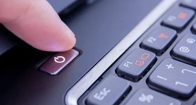 Ngón tay nhấn nút nguồn trên laptop, tượng trưng cho hành động bật hoặc tắt máy tính