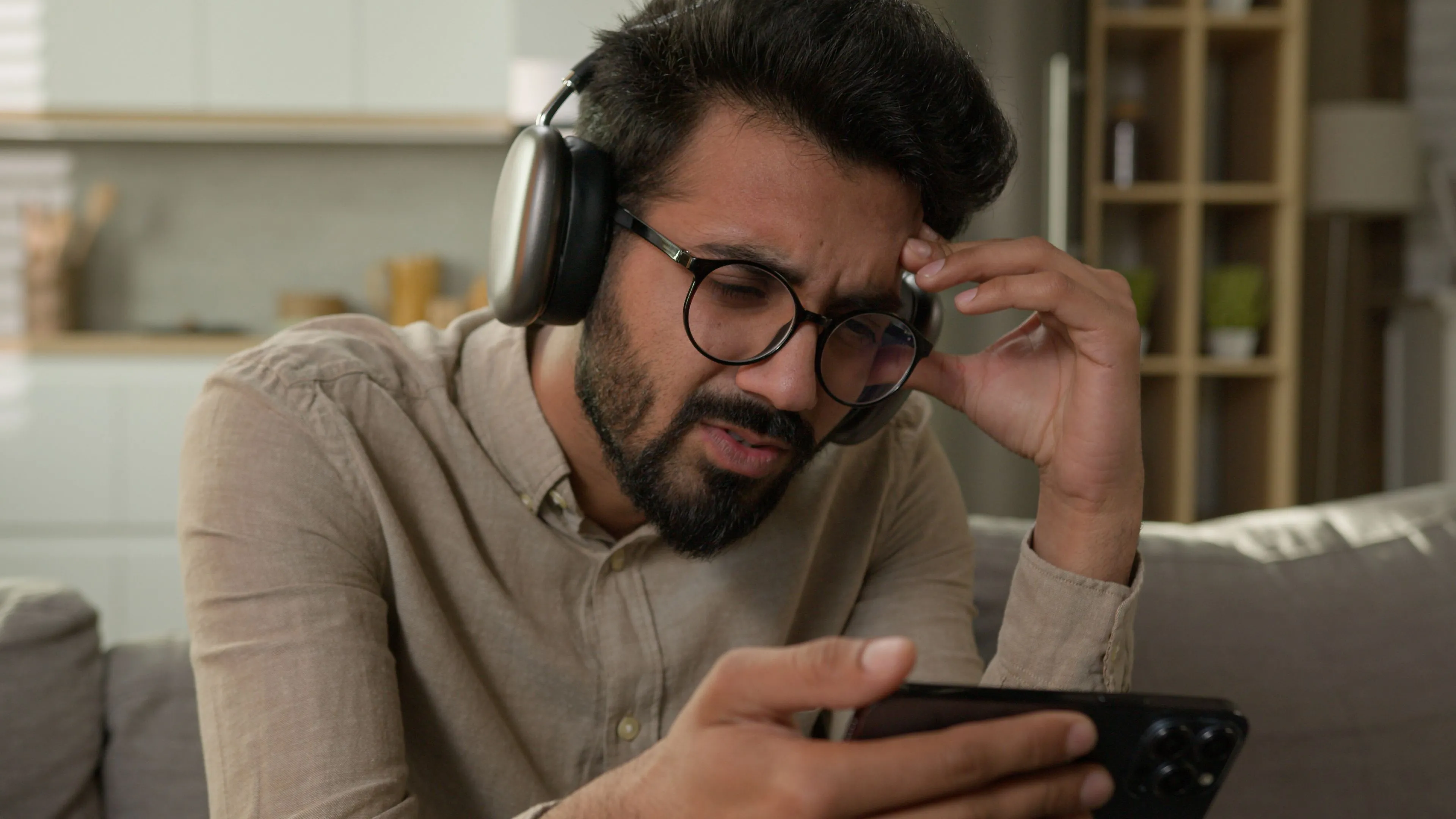 Người dùng di động nhìn iPhone với tai nghe AirPods Max, thể hiện sự lo lắng về việc chơi game gacha tốn kém