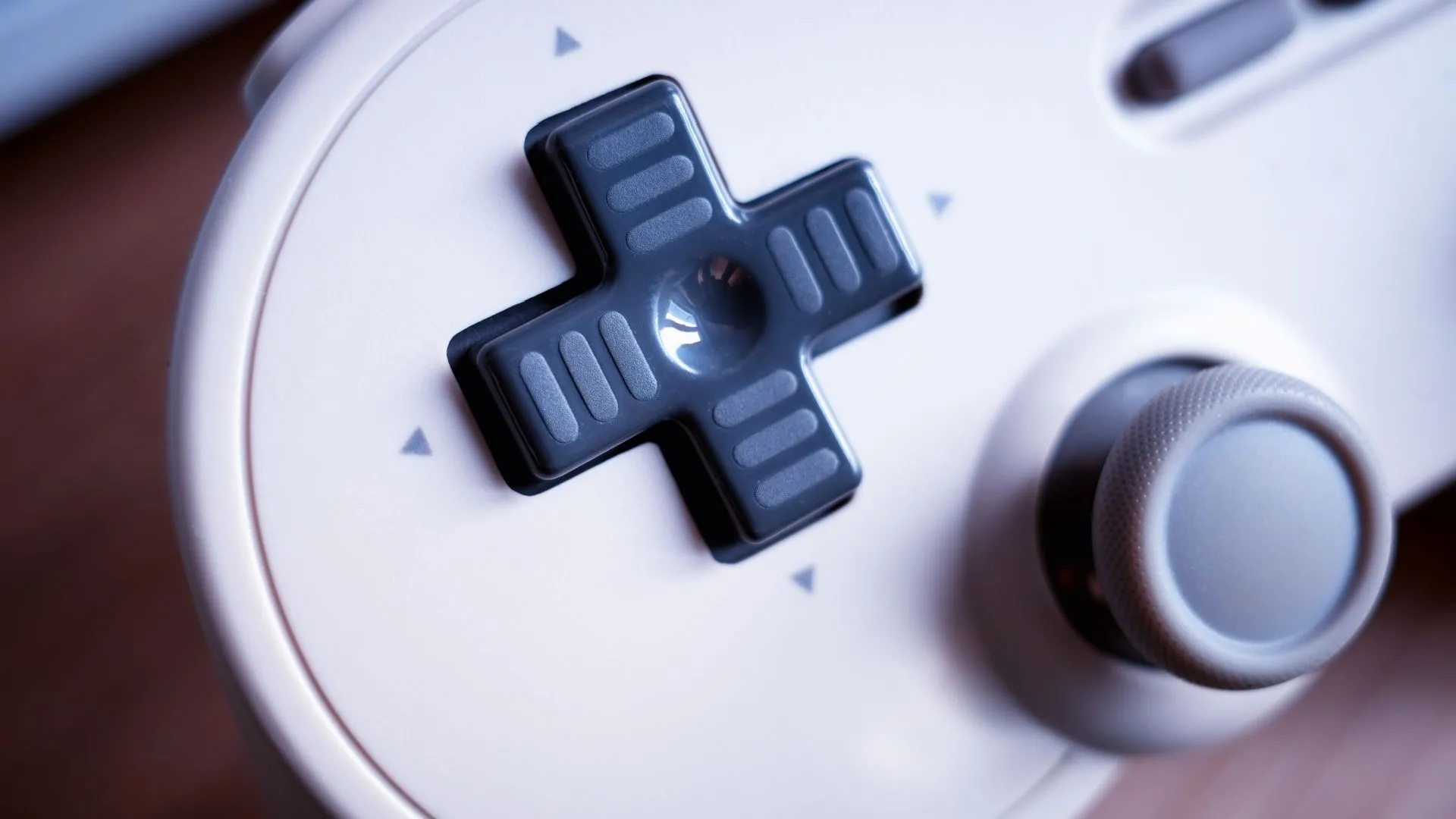Tay cầm gamepad cổ điển với D-Pad nổi bật ở chế độ cận cảnh, nền mờ ảo.