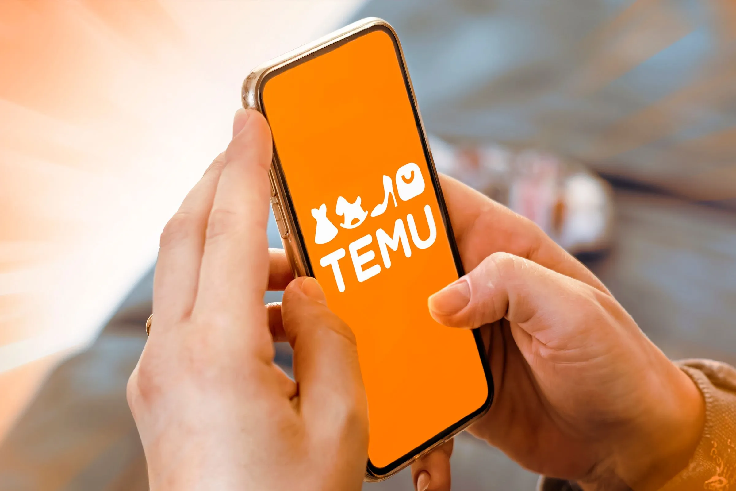 Bàn tay cầm điện thoại thông minh hiển thị logo Temu, minh họa ứng dụng Temu và trải nghiệm người dùng