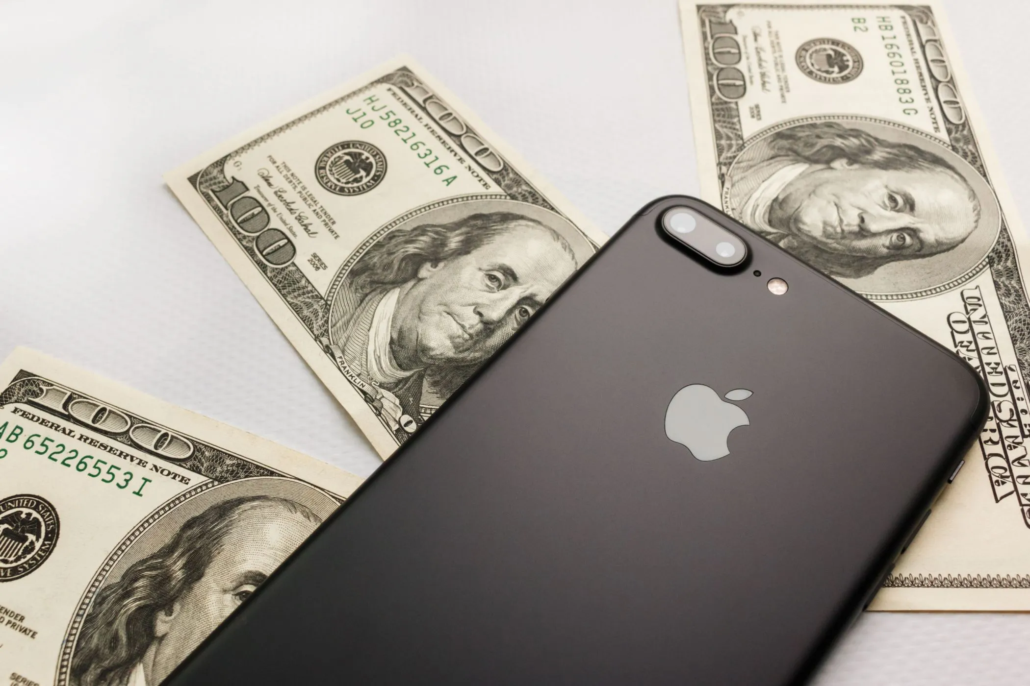 Chiếc điện thoại iPhone đặt trên nhiều tờ đô la, tượng trưng cho việc chi tiêu quá mức vào gacha game hoặc các giao dịch nhỏ