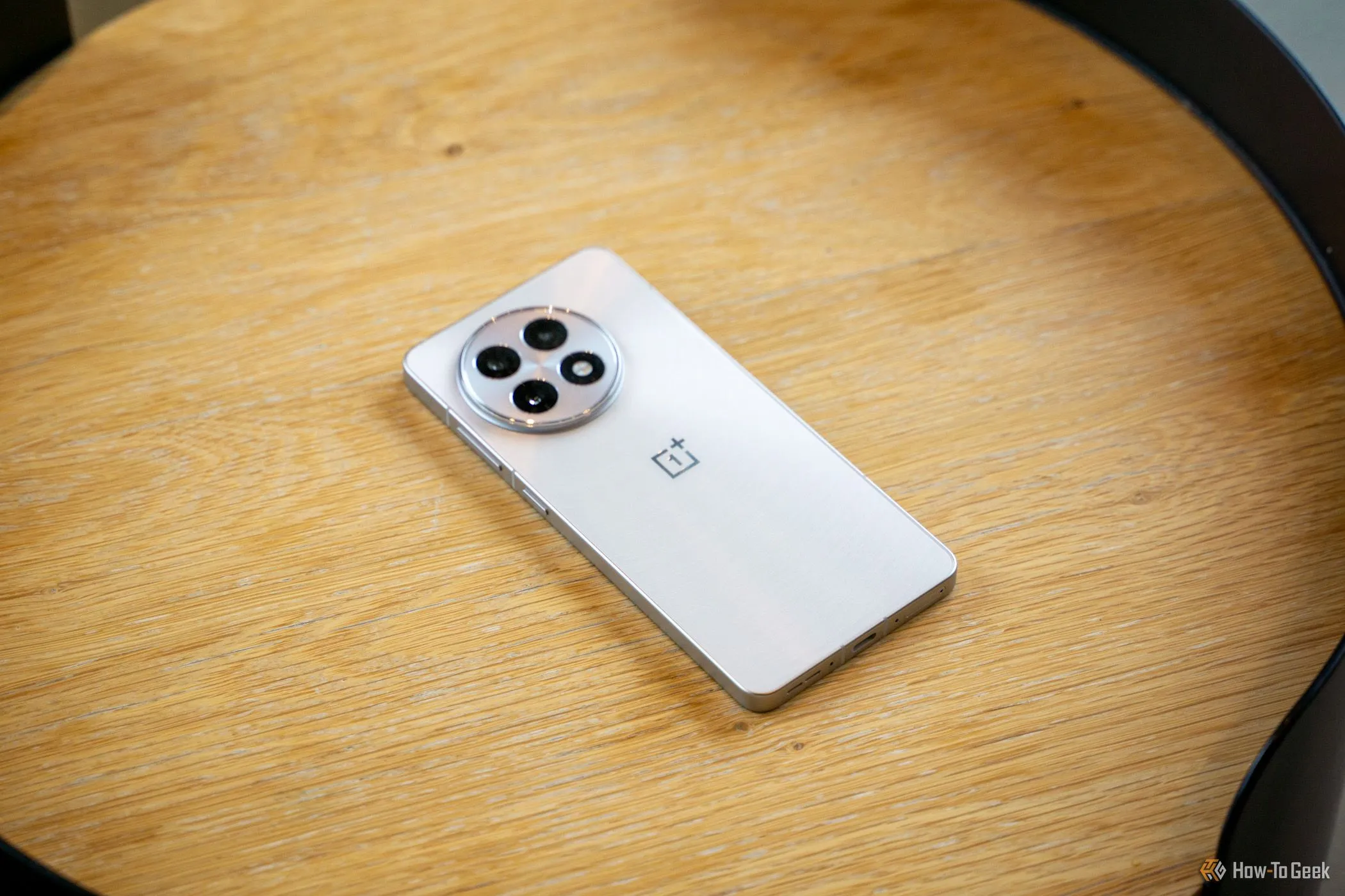 Điện thoại OnePlus 13R đặt úp mặt sau trên bàn gỗ, khoe cụm camera nổi bật.