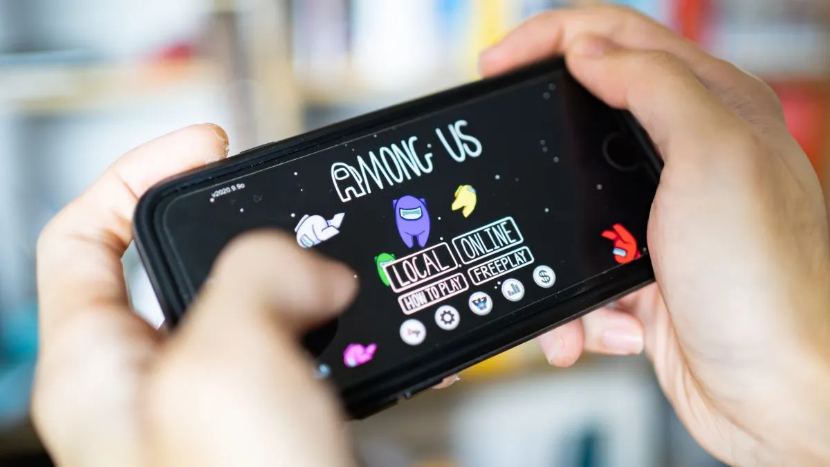 Đôi tay đang chơi game Among Us trên điện thoại thông minh, minh họa cho trải nghiệm game di động và chế độ co-op.