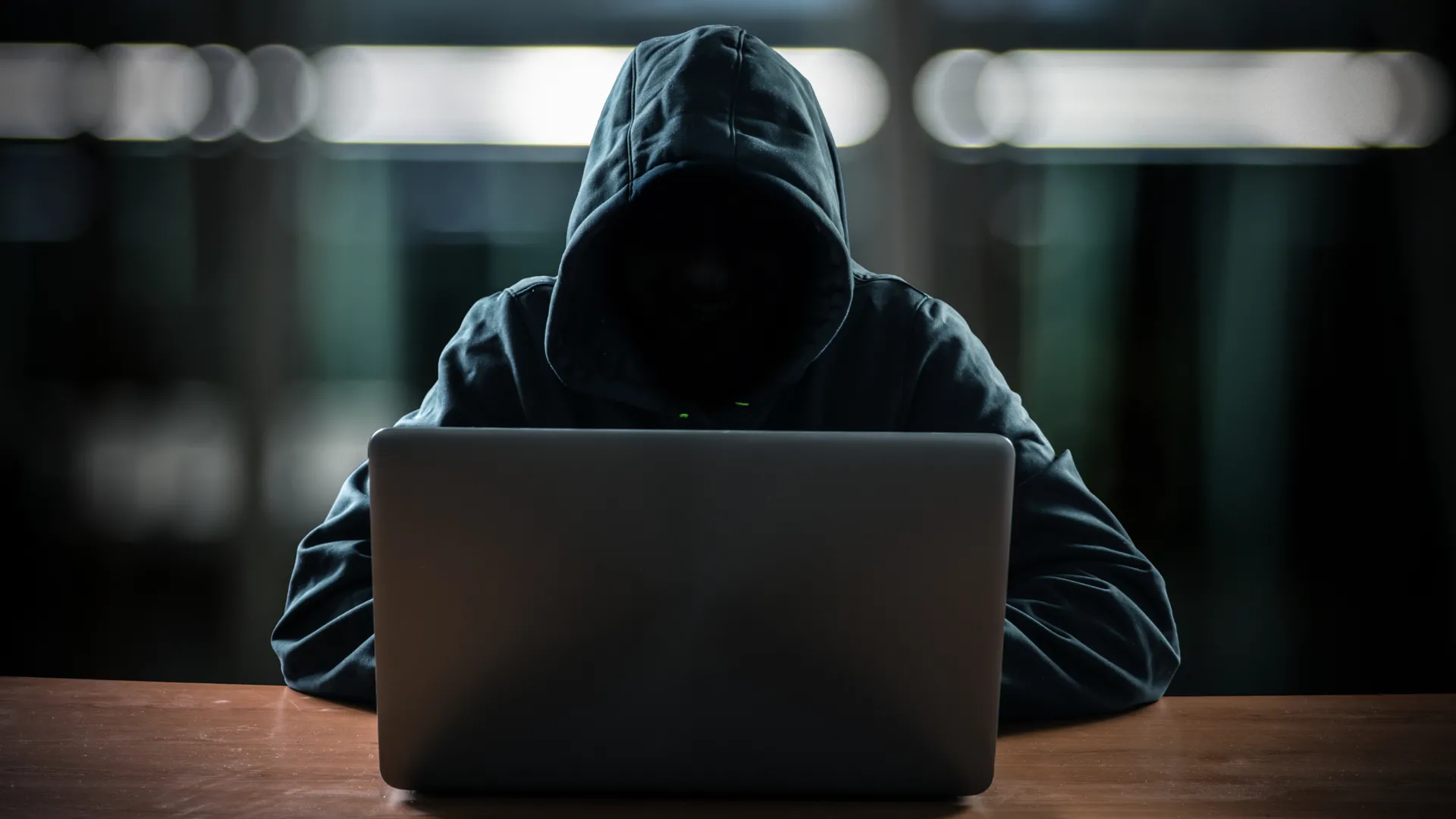 Hacker ngồi trước máy tính với gương mặt ẩn trong bóng tối.