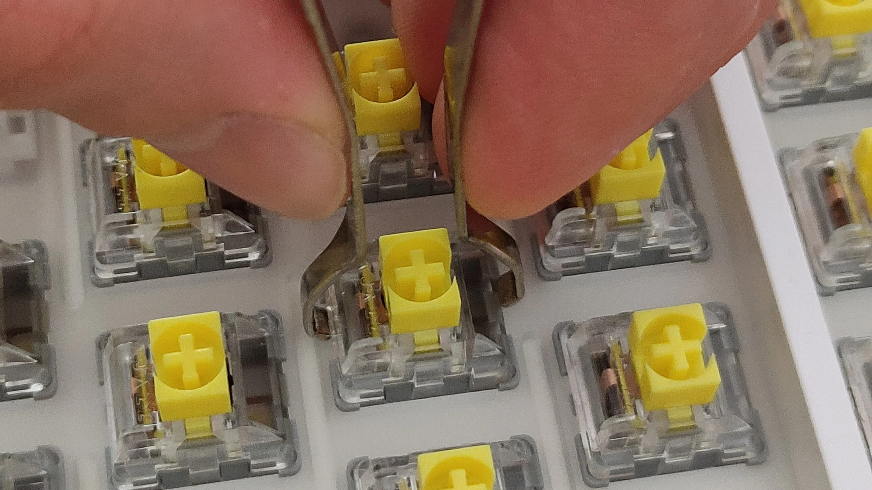 Hình ảnh cận cảnh một bàn tay đang tháo switch bàn phím cơ bằng dụng cụ chuyên dụng, minh họa khả năng tùy biến và sửa chữa