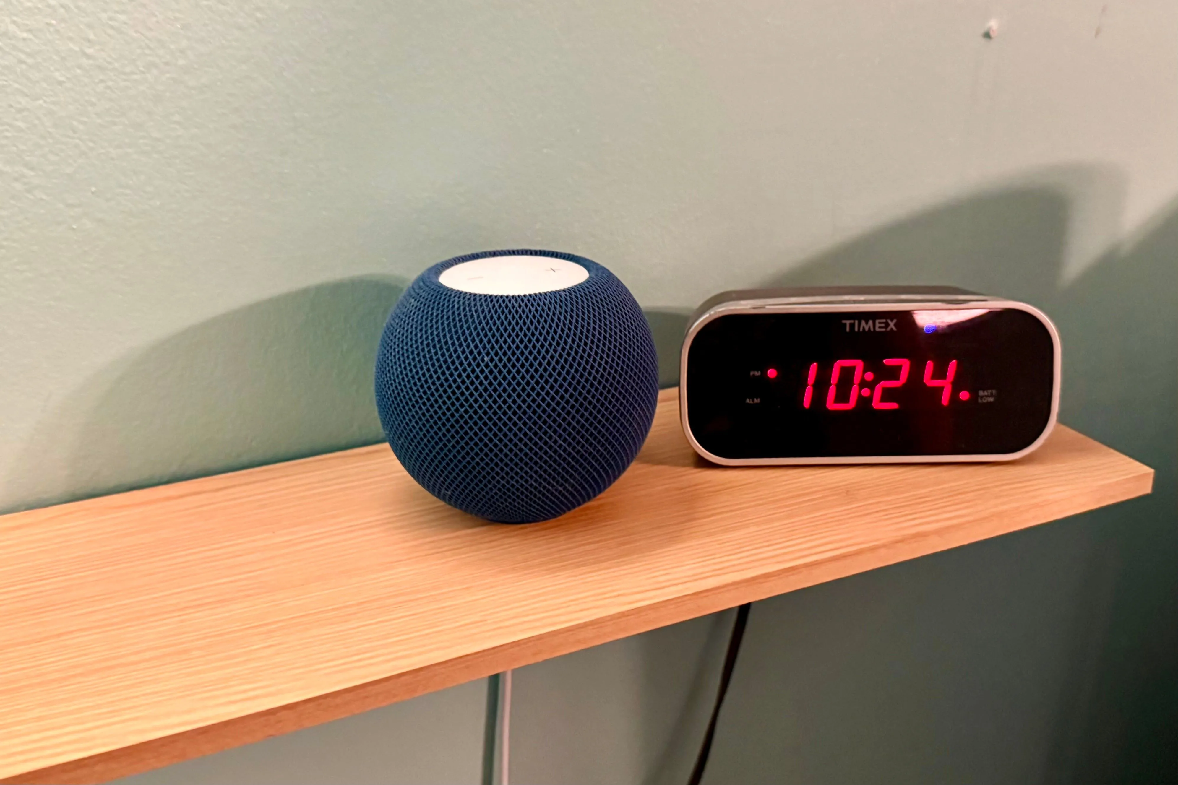 Loa thông minh HomePod mini trên kệ cạnh đồng hồ điện tử