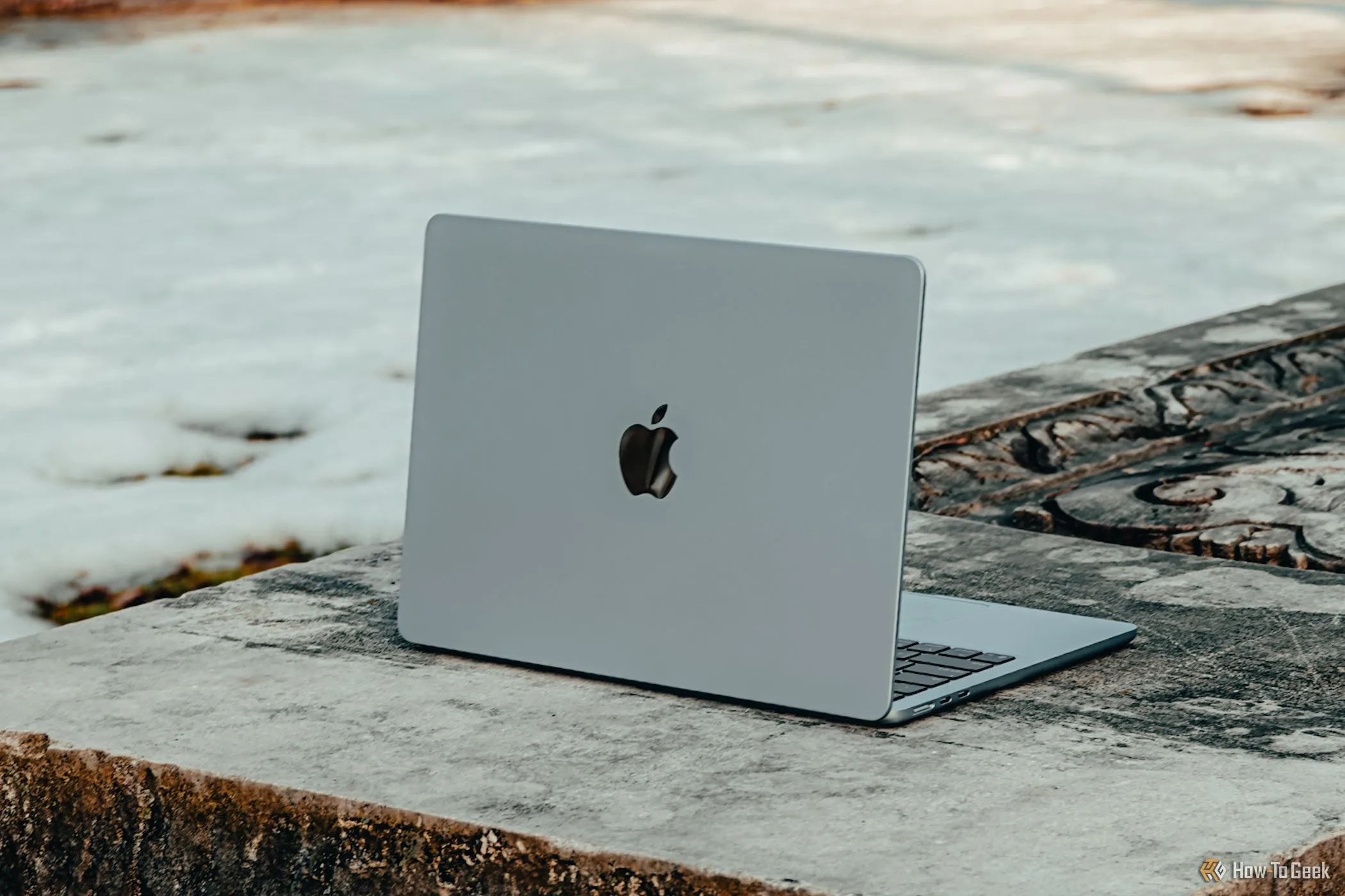 MacBook Air M4 màu xanh da trời được đặt nghiêng trên một chiếc ghế đá, thể hiện thiết kế hiện đại.