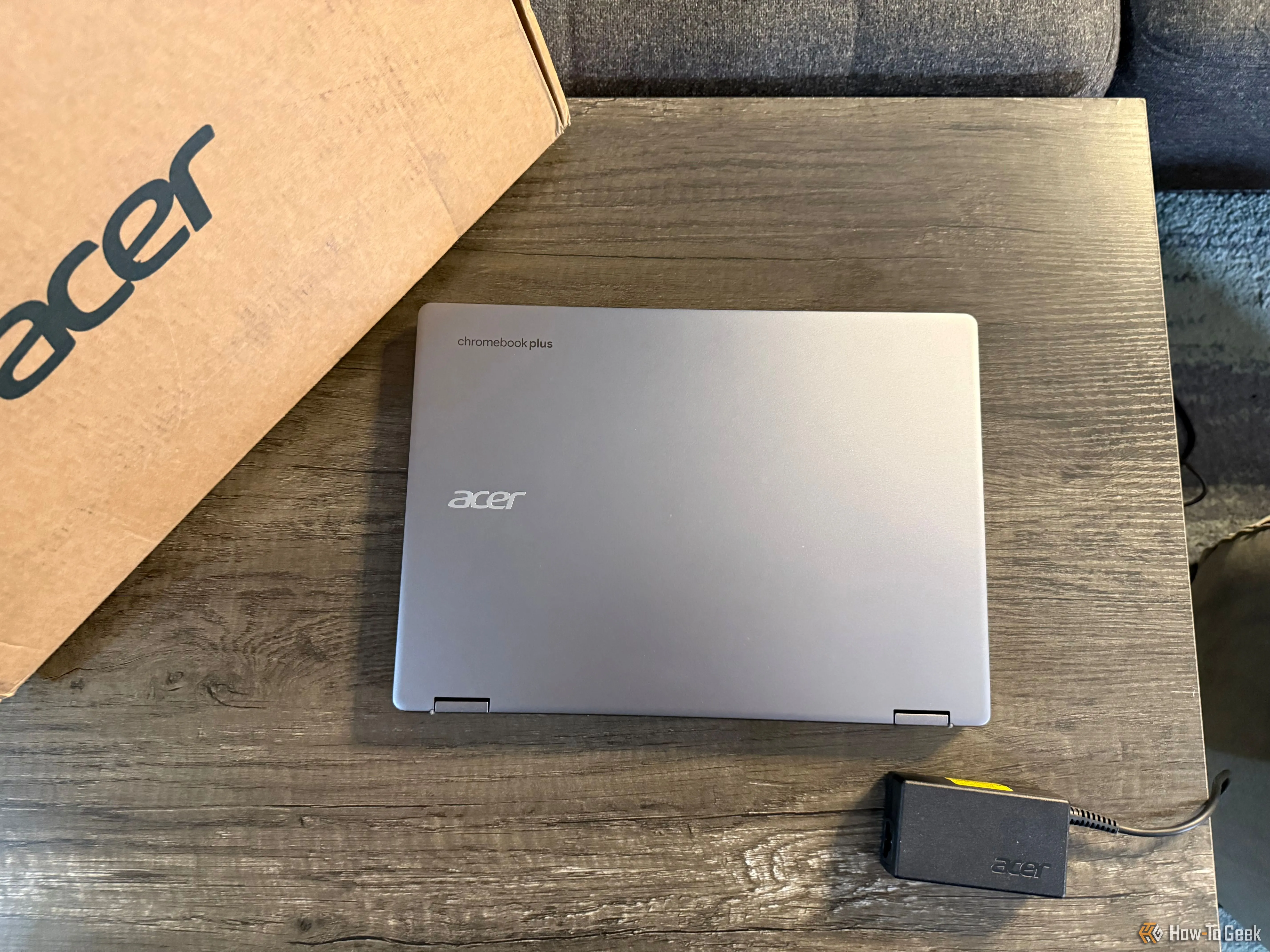 Máy tính xách tay 2 trong 1 Acer Chromebook Plus Spin 514 gập lại trên bàn cùng với hộp và bộ sạc.