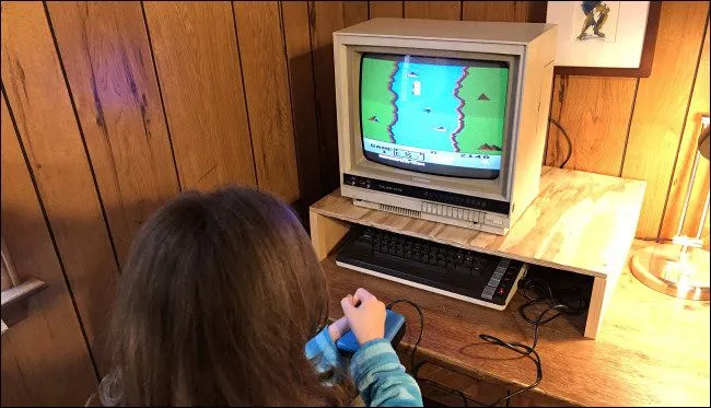 Một đứa trẻ đang chơi game River Raid trên máy tính Atari 800XL, thể hiện đồ họa pixel nghệ thuật của thập niên 80.