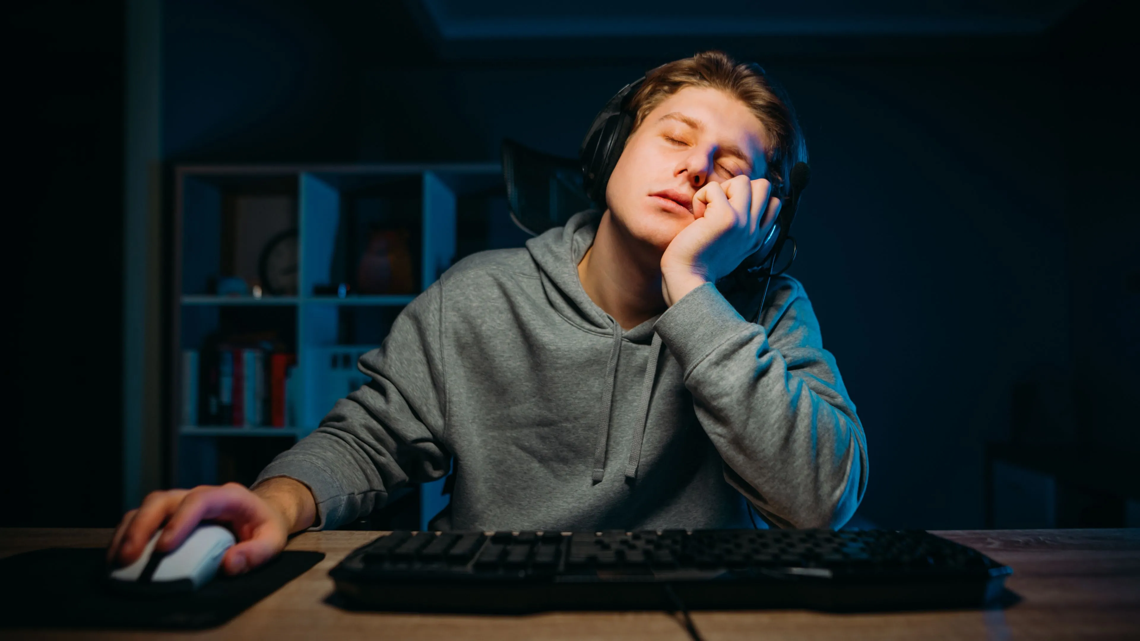 Một game thủ buồn ngủ đang gật gù trước máy tính, minh họa cho mong muốn có chế độ ngủ tức thì như thiết bị công nghệ.