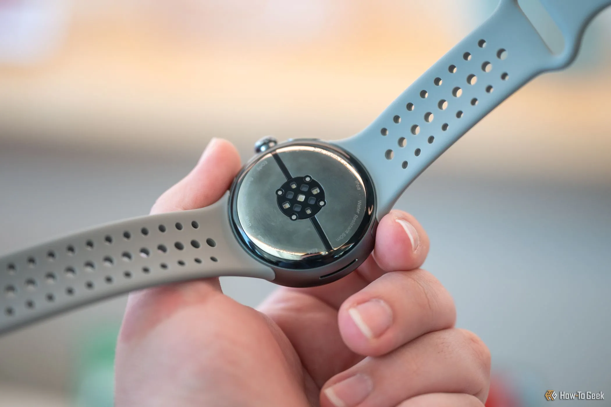 Một người đang cầm Google Pixel Watch 3 để lộ các cảm biến ở mặt dưới, minh họa thiết kế thân máy.