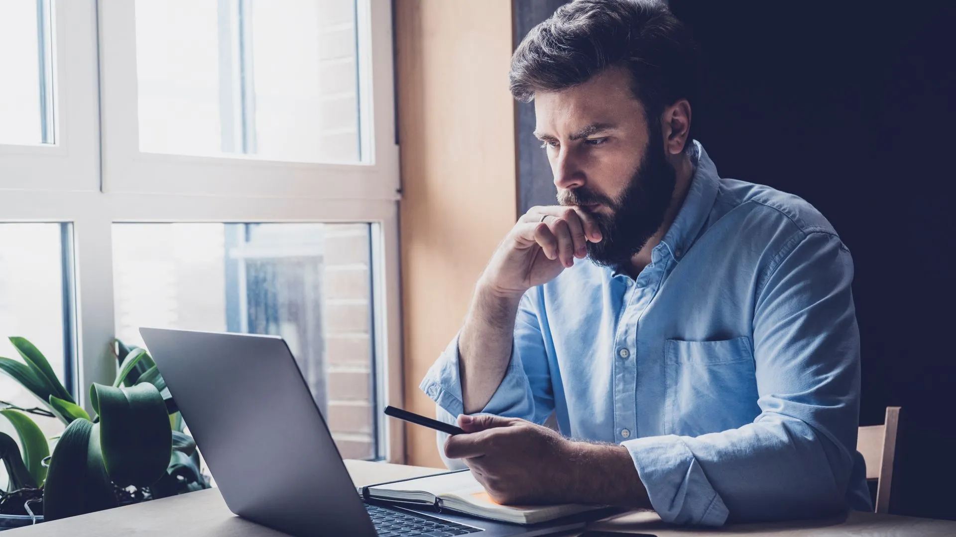 Người đàn ông suy nghĩ nghiêm túc khi làm việc trên laptop, tượng trưng cho uy tín chuyên nghiệp khi sở hữu website riêng.