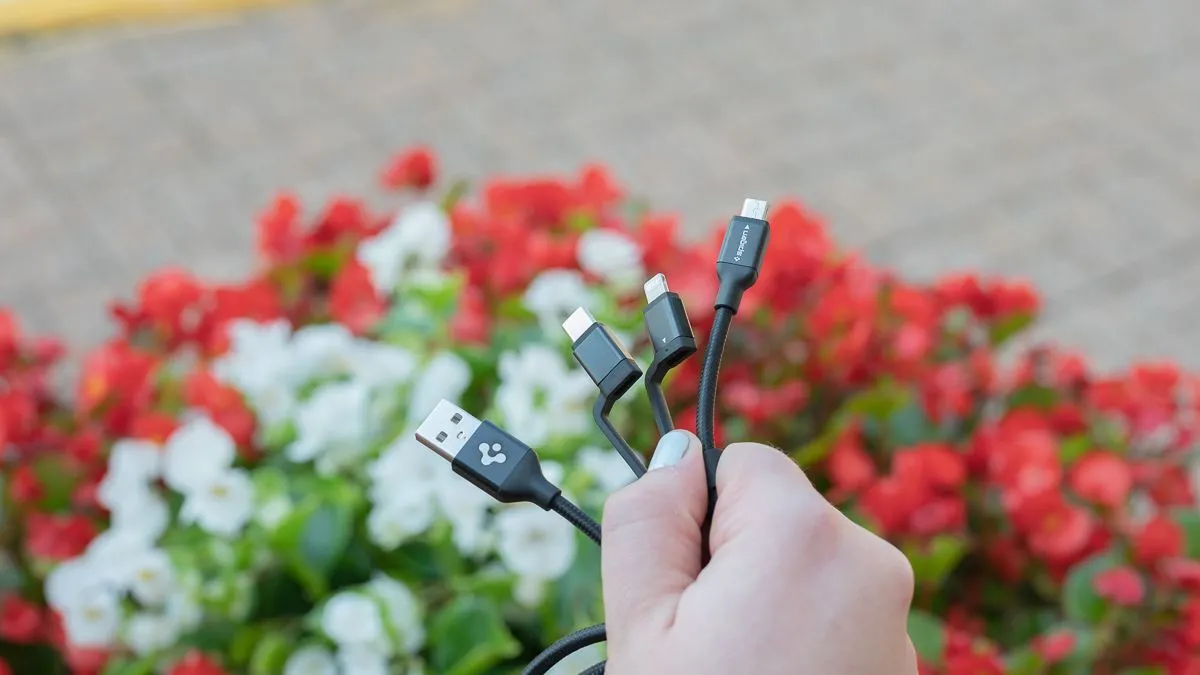 Người dùng đang cầm cáp sạc đa năng Spigen DuraSync 3-in-1, thể hiện các đầu nối khác nhau