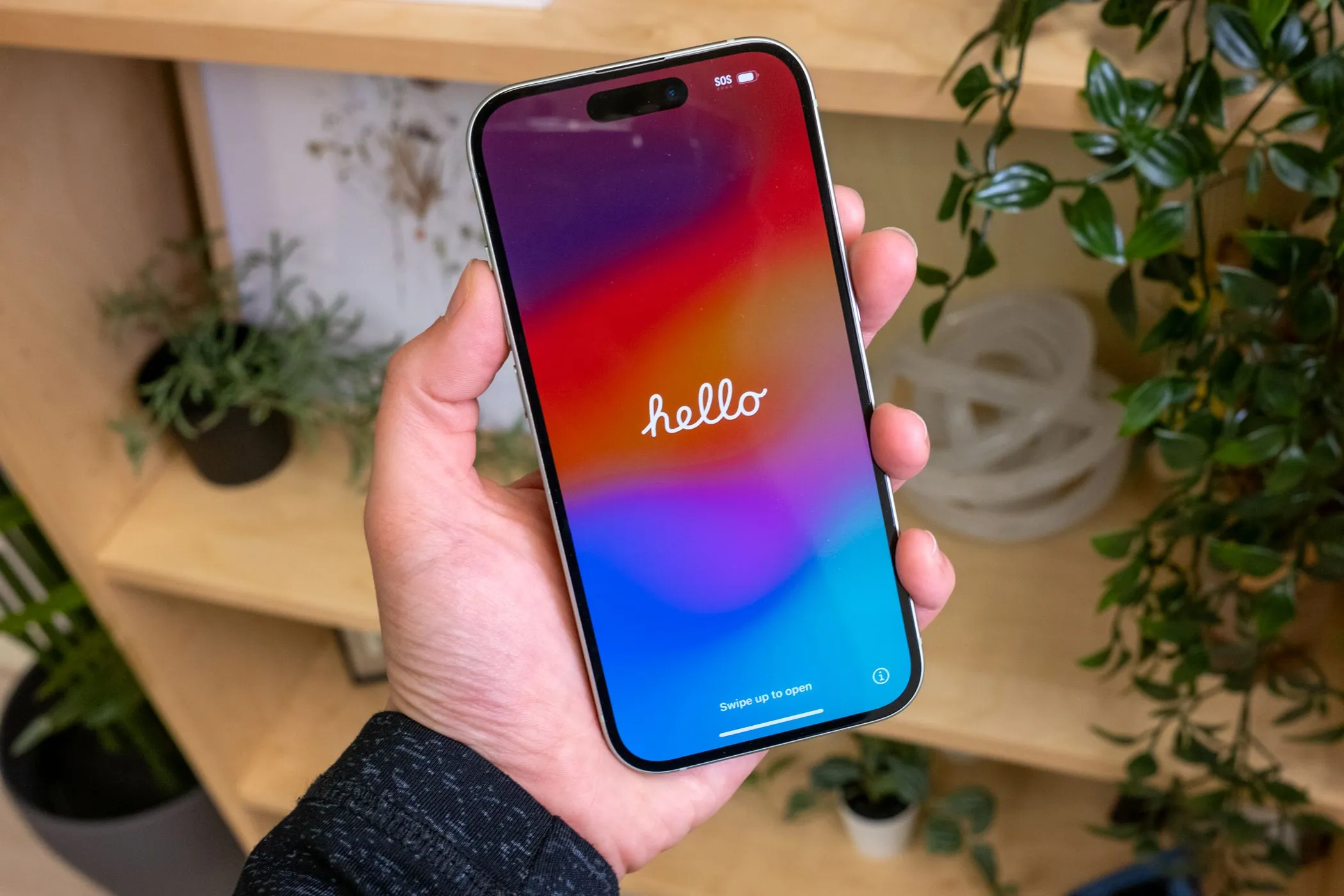 Người dùng đang cầm chiếc iPhone 15 màu xanh lá với màn hình hiển thị lời chào.