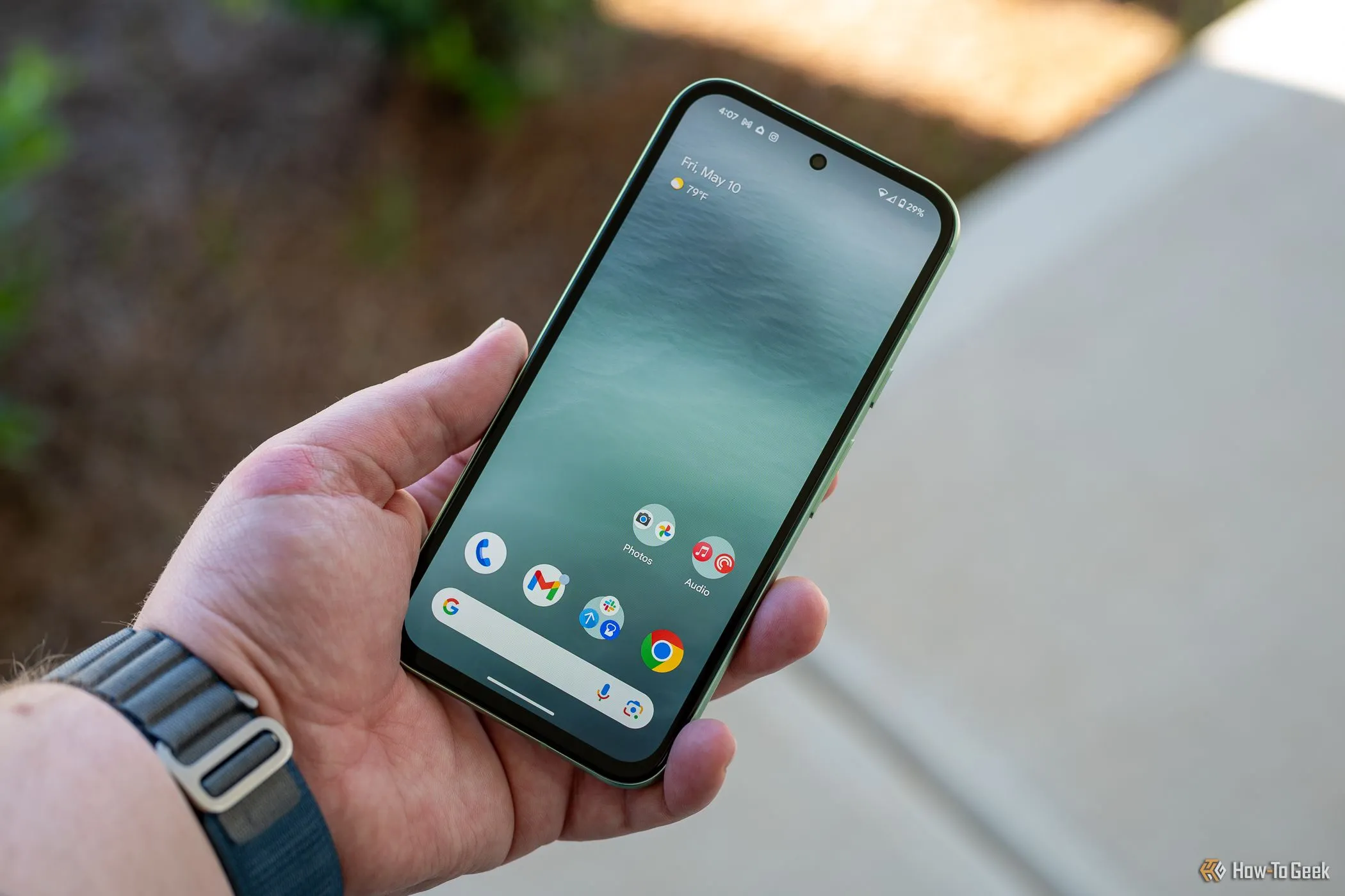 Người dùng đang cầm Google Pixel 8a hiển thị màn hình chính và viền máy.