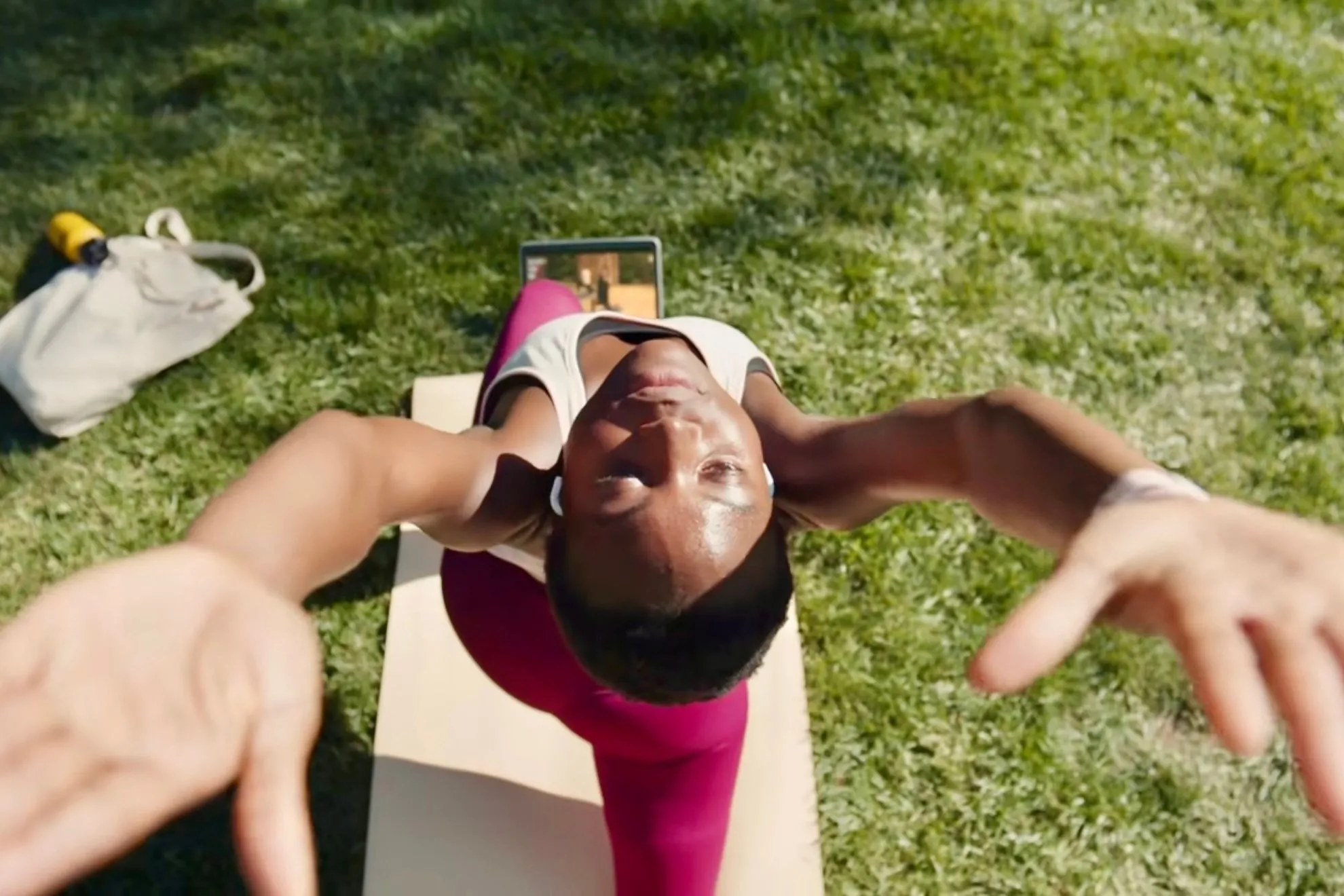 Người dùng tập yoga với Apple Fitness+ trong công viên bằng iPad và thảm tập.