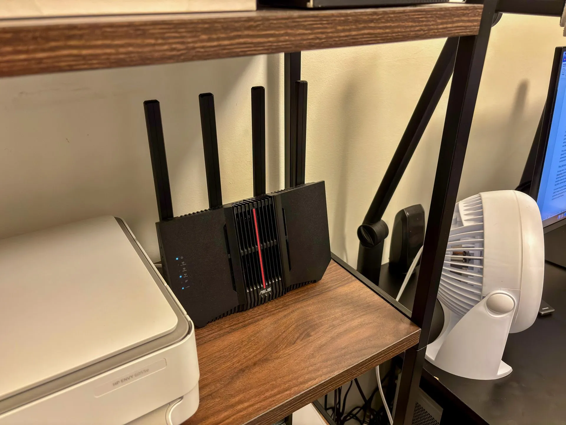 Router ASUS RT-BE92U Wi-Fi 7 được đặt trên kệ, kết nối với máy in và màn hình máy tính trong khu vực văn phòng.