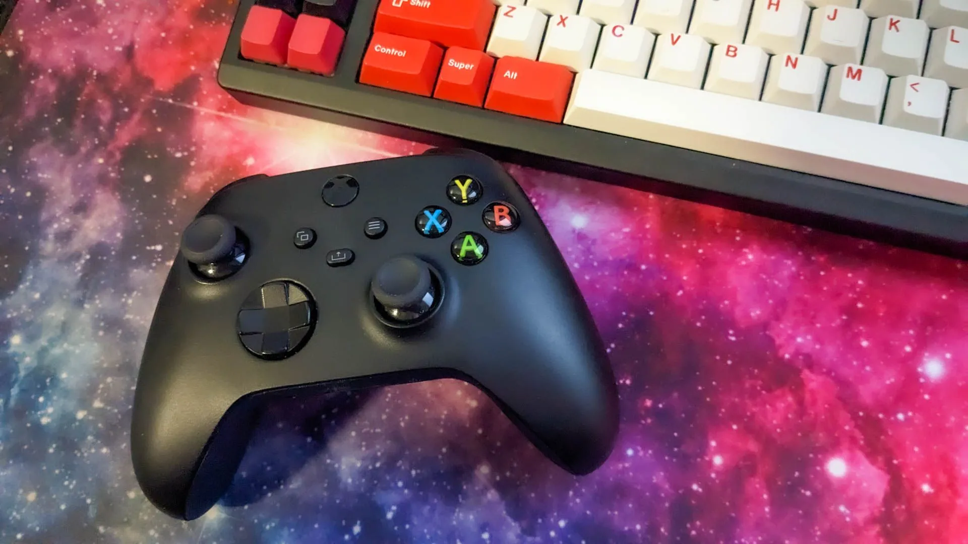 Tay cầm Xbox cạnh bàn phím cơ và chuột trên miếng lót chuột không gian