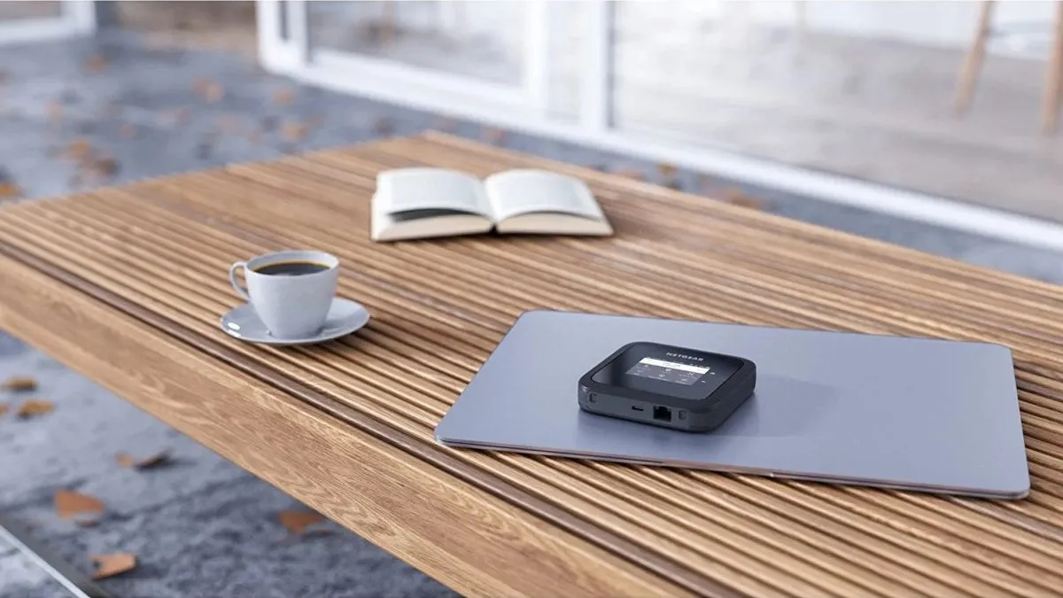 Thiết bị phát Wi-Fi di động Netgear Nighthawk M6 MR6150 màu đen đặt trên bàn gỗ ngoài trời, với đèn báo trạng thái hiển thị rõ ràng, thể hiện khả năng kết nối không dây mạnh mẽ cho người dùng di chuyển.