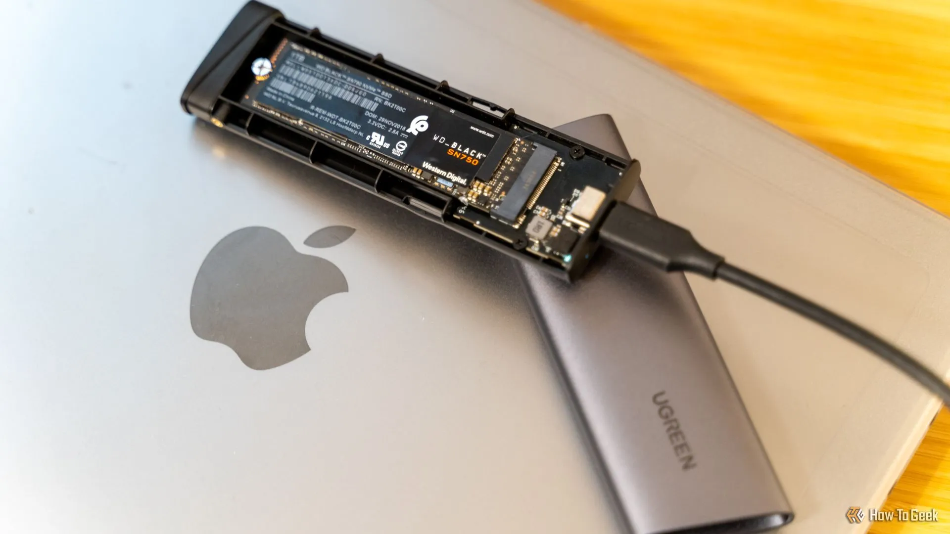 Vỏ bọc UGREEN M.2 NVMe SSD USB-C chứa ổ WD_BLACK SN750 đang kết nối với MacBook, thể hiện giải pháp lưu trữ di động.