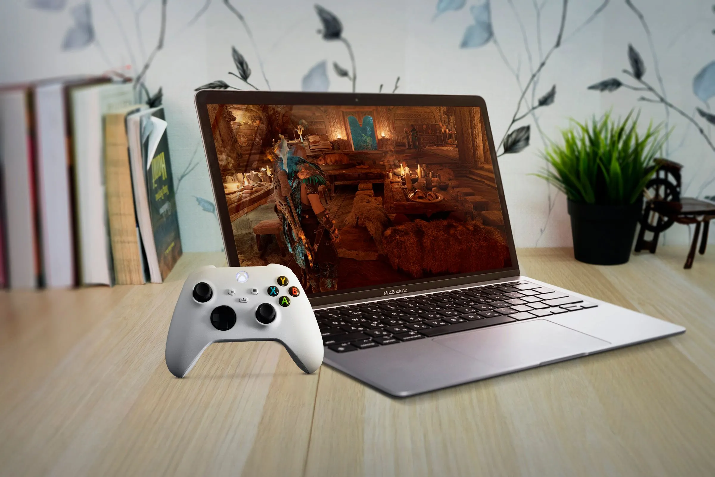 MacBook Air trên bàn gỗ với màn hình hiển thị game và tay cầm Xbox