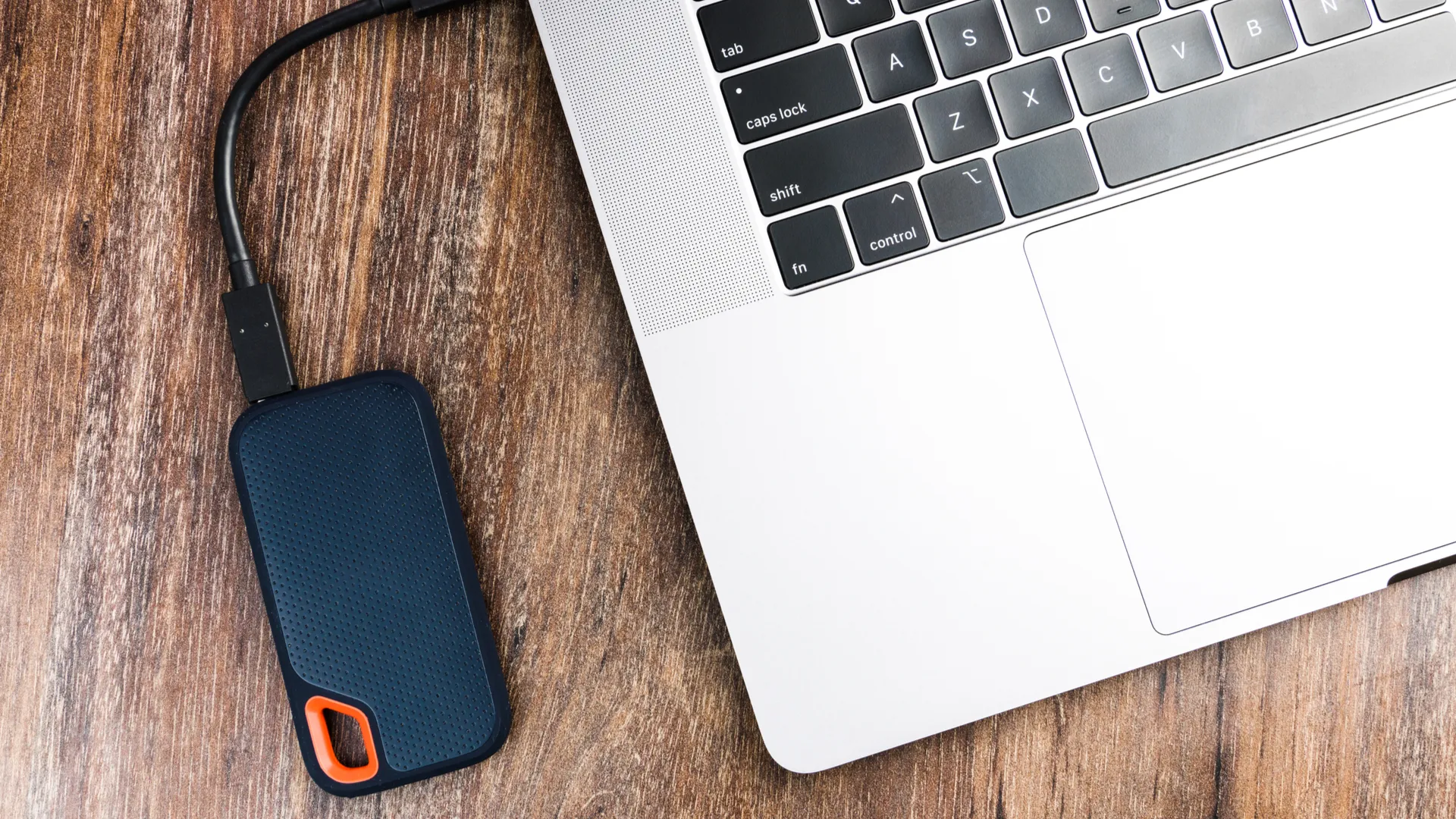 Ổ cứng SSD gắn ngoài và máy tính trên nền gỗ, biểu tượng của việc sao lưu dữ liệu cho Mac.