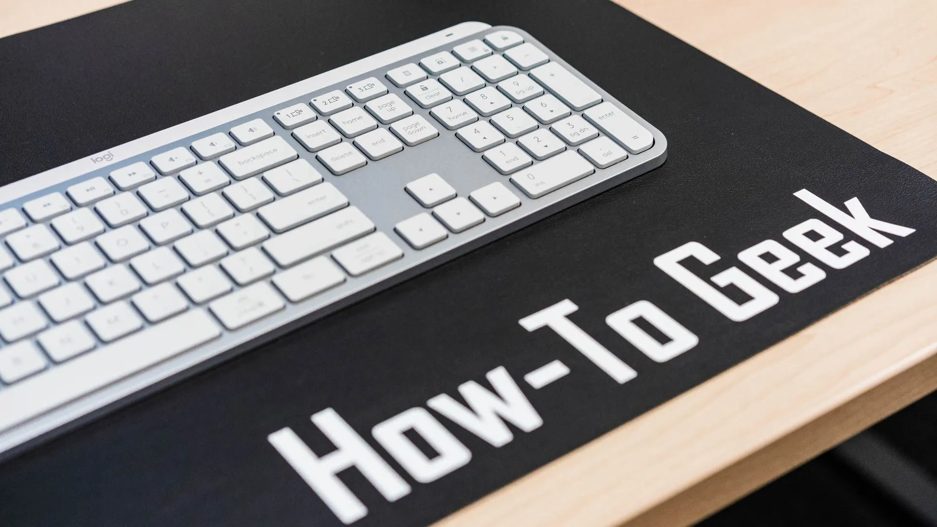 Phím Start trên bàn phím Logitech MX Keys S đặt trên tấm lót bàn How-To Geek, làm nổi bật thiết kế sang trọng và chuyên nghiệp.