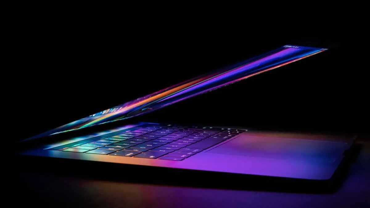 Một chiếc MacBook nửa gập với màn hình phản chiếu màu sắc sống động lên bàn phím